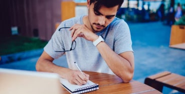 A postgraduate student writing revision notes in a notepad