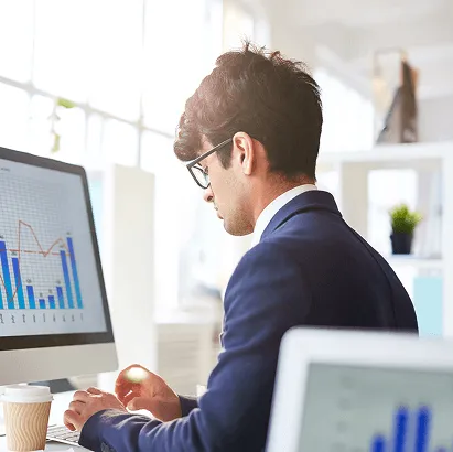 Professional reviewing data charts on a desktop computer in an office.