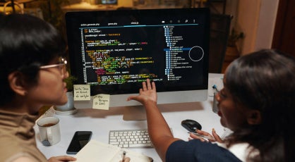 Two data professionals discussing programming code on a monitor.