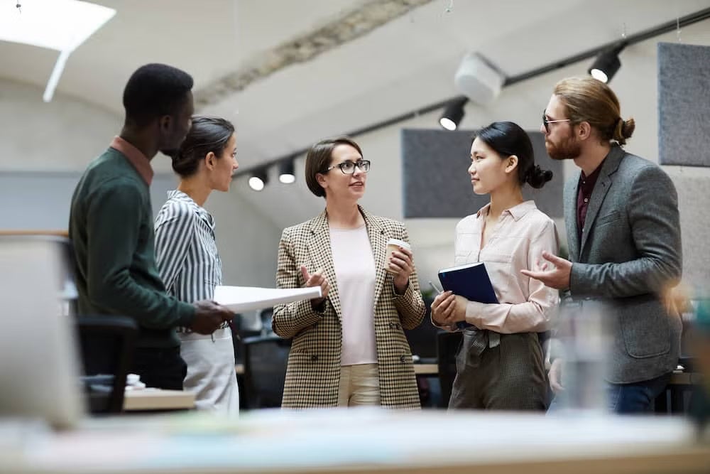 A group of diverse individuals standing together in a modern office environment, engaged in conversation.