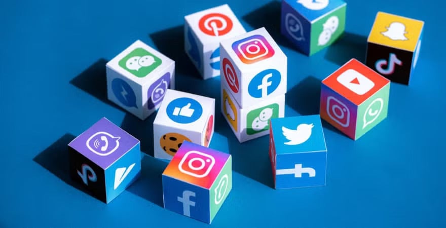 Colorful cubes featuring popular social media app icons such as Facebook, Instagram, Twitter, TikTok, Snapchat, and YouTube are scattered on a blue surface.